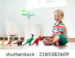 Small photo of Child playing with colorful toy dinosaurs. Educational toys for kids. Little boy learning fossils and reptiles. Children play with dinosaur toys. Evolution and paleontology game for young kid.