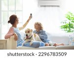 Mother and child with air conditioner remote control. Comfortable temperature at family home. Cooling and heating device. Mom and kid on couch under cold breeze. Air conditioning on hot summer day. 