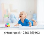 Small photo of Adorable baby boy learning to crawl and playing with colorful rainbow ball toy in white sunny bedroom. Cute laughing child crawling on a play mat. Nursery, clothing and toys for little kids.