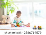 Small photo of Adorable Asian baby boy learning to crawl and playing with colorful block toy in white sunny bedroom. Cute laughing child crawling on a play mat. Nursery, clothing and toys for little kids.