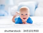 Adorable baby boy in white sunny bedroom. Newborn child relaxing in bed. Nursery for young children. Textile and bedding for kids. Family morning at home. New born kid during tummy time with toy bear.