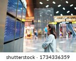 Woman in virus protection face mask looking at information board checking her flight in international airport. Departure board, flight status                             