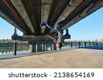 Small photo of Young man break dancer doing somersault acrobatic stunts dancing on urban background. Street artist breakdancing outdoors