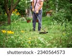 Close up of young man cutting grass with weed cutter on his grassy lawn. Gardening concept