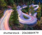 The mountain pass of Maloja, Switzerland. A road with many curves among the forest. A blur of car lights. Landscape in evening time. Large resolution photo for design.