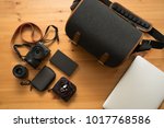 Black digital camera with orange leather strap on the wooden table with navy bag, laptop and notebook.