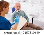 Small photo of Senior man having dental checkup at dentist office, consulting with doctor about necessary procedures, dentist taking medical records