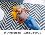 Top view of beautiful young woman lying on the living room floor wearing headset listening to an audio book and relaxing at home, enjoying her leisure time alone