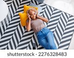 Top view of beautiful young woman lying on the living room floor wearing headset listening to the music and relaxing at home, enjoying her leisure time alone