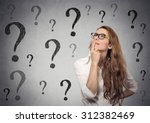 Thinking business woman with glasses looking up on many questions mark isolated on gray wall background