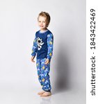 Small photo of Frolic smiling blond 5-6 y.o. kid boy in pyjamas with african animals pattern and map print stands side to camera looking at us is getting ready for bed, going to sleep over gray background