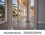 Columns and marble floor of the Ghagra Colonnade at sunset. The historical architectural structure opens the scenic view of the Black Sea and its coast with palms. Landscapes, travel, tourism.