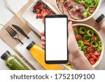 Small photo of Hand of woman hold phone mock up white screen over weight loss diet fresh healthy food take away boxes bag daily nutrition ready menu plan meal online delivery service mobile app ad. Flat lay top view
