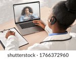 Small photo of African doctor wear headset consult female black patient make online webcam video call on laptop screen. Telemedicine videoconference remote computer app virtual meeting. Over shoulder videocall view.