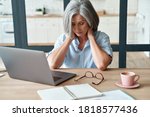 Small photo of Tired stressed old mature business woman suffering from neckpain working from home office sitting at table. Overworked senior middle aged lady massaging neck feeling hurt pain from incorrect posture.