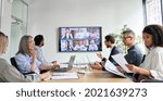 Small photo of Diverse company employees having online business conference video call on tv screen monitor in board meeting room. Videoconference presentation, global virtual group corporate training concept.