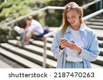 Young smiling woman university student holding cell phone using mobile apps technology on smartphone looking at cellphone texting in messengers writing messages standing outside campus.