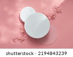 White round podium pedestal cosmetic beauty product presentation empty mockup on trendy pink coral pastel background with light shadows and spring flowers, minimalist flat lay backdrop, top view.