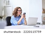 Small photo of Young happy business woman, smiling beautiful professional lady worker looking at smartphone using cellphone mobile cellular tech working at home or in office checking cell phone sitting at desk.