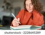 Business woman or young female student holding pen in hand writing in paper notebook journal, taking notes studying, doing homework, making checklist. Close up view