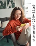 Small photo of Young pretty woman holding smartphone using cellphone modern technology, looking at mobile, checking cell phone apps, texting typing messages, browsing internet for shopping sitting at home. Vertical