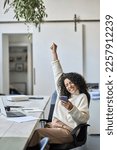 Small photo of Euphoric young female worker holding mobile phone celebrating win receiving good news about job promotion, getting hired, feeling happy, rejoicing success with yes reaction working in office. Vertical