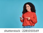 Young happy excited latin woman pointing at mobile phone isolated on blue background. Smiling female model holding cellphone using cell presenting advertising new trendy application concept.