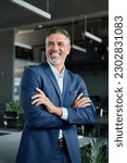 Small photo of Happy confident middle aged business man, mature professional ceo corporate leader wearing blue suit standing in modern office with arms crossed looking away laughing, authentic vertical portrait.