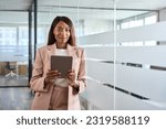 Small photo of Young professional African American business woman company manager sales executive wearing suit holding fintech tab digital tablet computer standing in office at work, looking at camera, portrait.