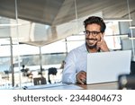 Happy Latin business man wearing glasses working at laptop in office looking away. Happy young male professional using computer sitting at desk thinking of corporate technology solutions. Copy space