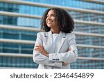 Happy young African American business woman standing in city looking away. Confident smiling confident professional businesswoman leader wearing suit thinking of success, dreaming of new goal outdoor.