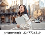 Small photo of Young busy happy Asian business woman office professional holding cellphone in hands walking on big city urban street making corporate business call, talking on the cellular phone. Authentic shot