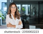 Small photo of Confident 45 year old Latin professional mid aged business woman corporate leader, mature female executive manager wearing eyeglasses standing in office arms crossed looking at camera, portrait.