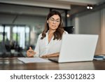 Small photo of Mid aged business woman having hybrid meeting working in office. Busy mature female corporate leader executive, hr manager communicating by conference call, remote online job interview on laptop.