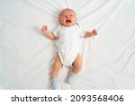 Small photo of a newborn baby cries on a white sheet. childish tantrums. colic and abdominal pain in infants. medicines and vitamins for babies. top view.