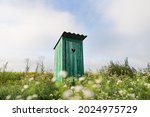 Vintage toilet. An outdoor rustic green toilet with a heart cut out on the door. Toilet in a field of flowers