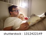 Father reading bedtime stories to child. Dad putting son to sleep. Quality family time.