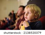 Small photo of Cute little boy with his father watching cartoon movie in the cinema or performance in viewer hall of theatre. Leisure entertainment for family with kids. Cultural event for children.