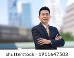 Portrait of successful asian businessman standing with arms crossed standing in front of modern office buildings