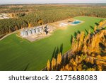 Small photo of Aerial view modern granary, grain-drying complex, commercial grain or seed silos in sunny autumn rural landscape. Corn dryer silos, inland grain terminal, grain elevators standing in a field in sunny