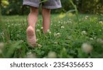 Small photo of girl walks on the grass barefoot in the park. happy family kid dream concept. bare feet close-up walks on the grass in summer lifestyle child. daughter walks barefoot on the grass in the park