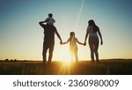 Small photo of people in the park. happy family walking silhouette at sunset. mom dad and daughters walk holding hands in park. happy family childhood dream concept. parents and children sun go back silhouette