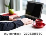 Man hands on laptop keyboard with red notebook, green apple and red cup of coffee on white table