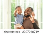 Small photo of Happy african black parents dad father throw baby son on piggyback and neck riding teasing fun near window. Black baby son and daddy enjoy teasing kiss cheek and neck riding at window light