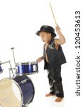 Small photo of An adorable, barefoot preschooler dressed as a rock star with a drum stick poised high over a drum set, ready to "wham" it. On a white background.