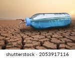 Full water of plastic bottle with water taps on dry cracked earth metaphor water crisis, scarcity and drought on summer. Lack of fresh water concept.