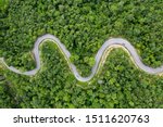 Aerial view of countryside road passing through the green forrest and mountain.