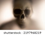 Small photo of Horror skeleton or grim reaper behind the matte glass. Halloween festival concept.Blurred picture