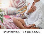 Self-Healing Heart Chakra Meditation. Woman sitting in a lotus position with right hand on heart chakra and left palm open in a receiving gesture. Self-Care Practice at Home