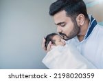 Small photo of Closeup portrait of young asian Indian father holding kissing his newborn baby with copy space. Healthcare and medical daycare nursery love lifestyle together single dad father’s day holiday concept